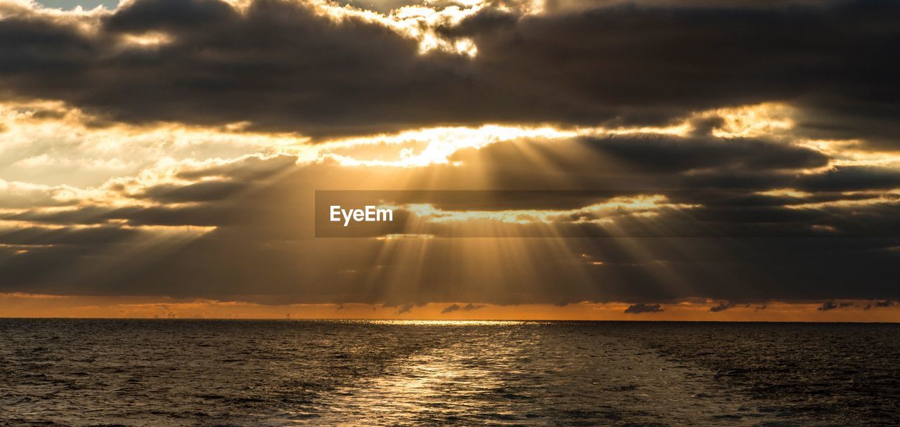 Sunlight streaming through clouds over sea at sunset