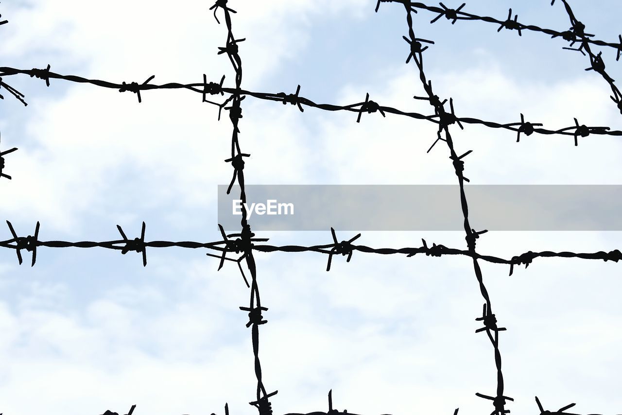Low angle view of barbed wire fence against cloudy sky