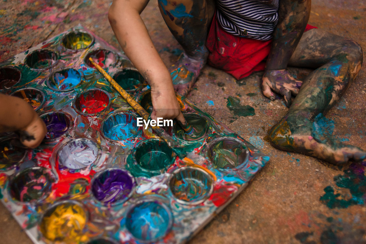 Low section of child playing with paint on a tray on te floor