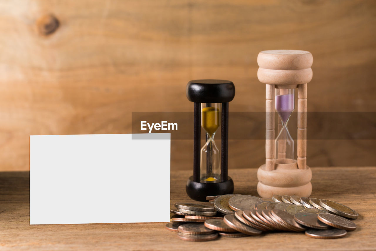 Close-up of blank paper with hourglasses and coins on wooden table