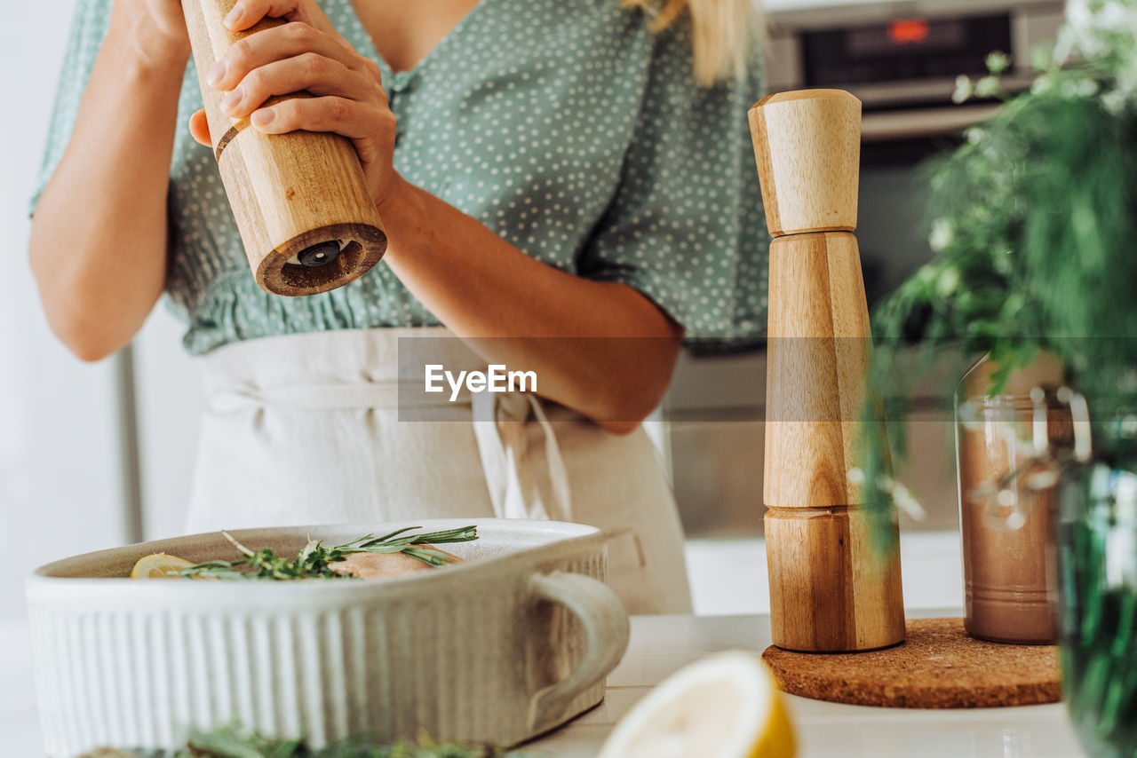 Woman with a pepper grinder seasoning food in a tray