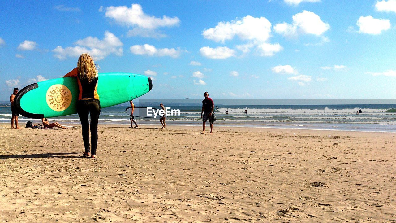 Rear view of woman holding surfboard at beach against sky