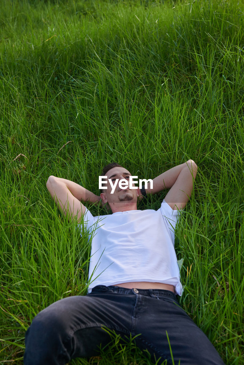 An attractive boy sleeping peacefully on the grass in a park.