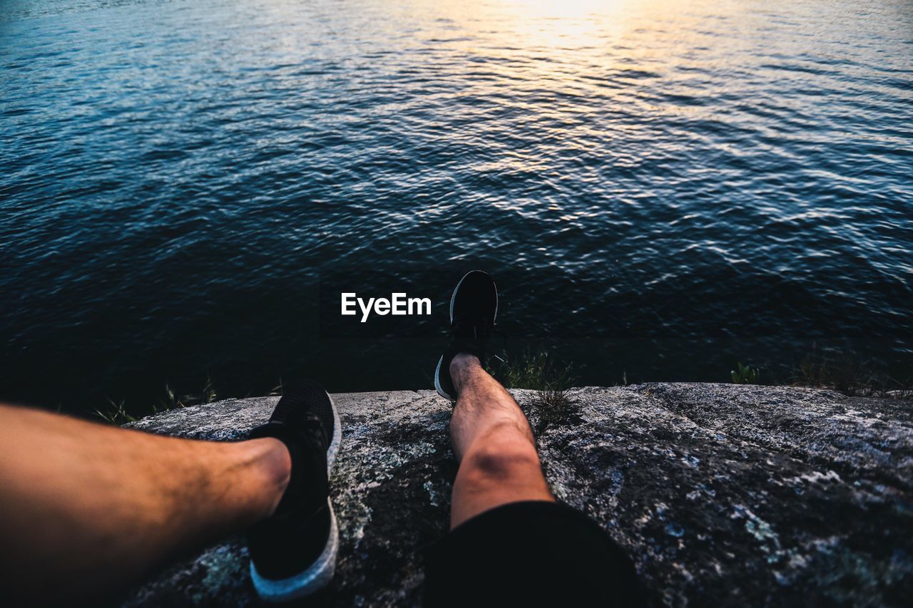 LOW SECTION OF MAN SITTING AT SEA SHORE