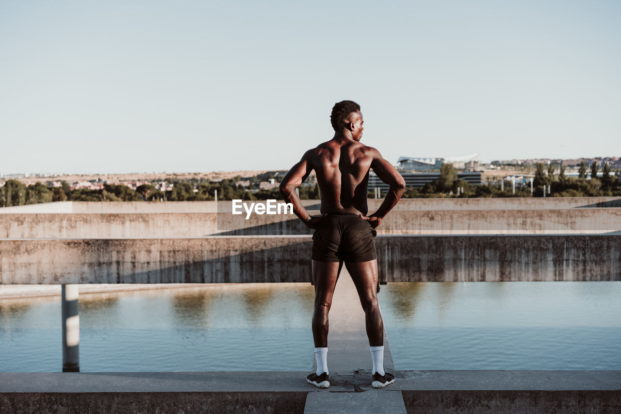 Male athlete with hand on hip standing against sky during sunny day