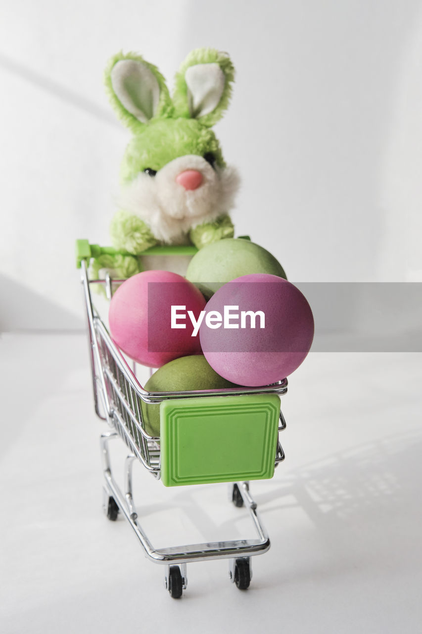 Toy soft green rabbit and  small shopping cart with colored natural chicken eggs. easter composition