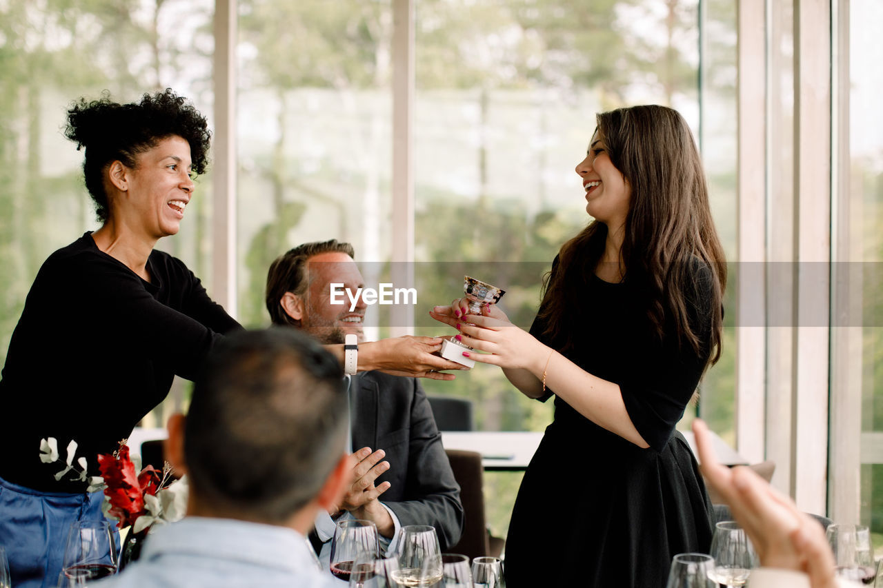 Smiling businesswoman giving trophy to female colleague during kick off meeting at convention center