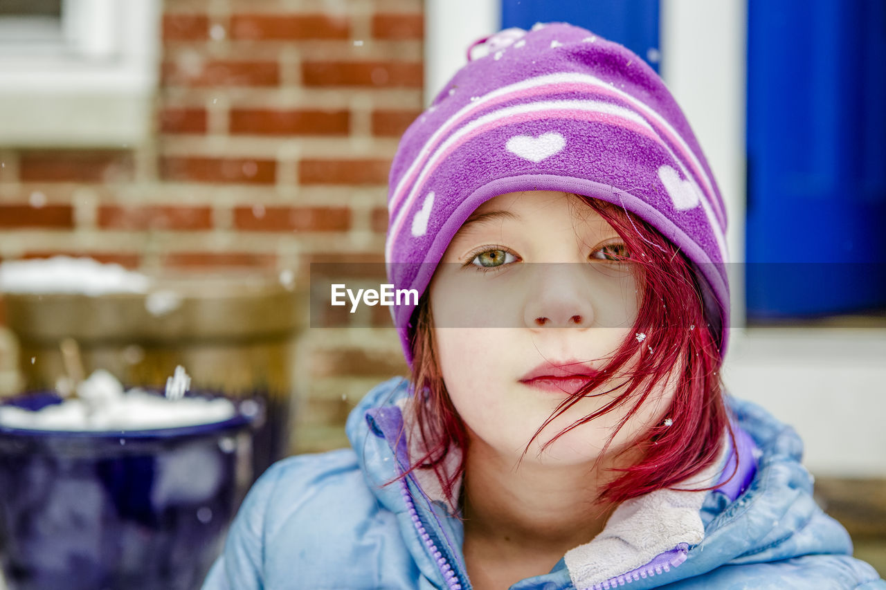 Beautiful little girl with bright red dyed hair sits outside in winter