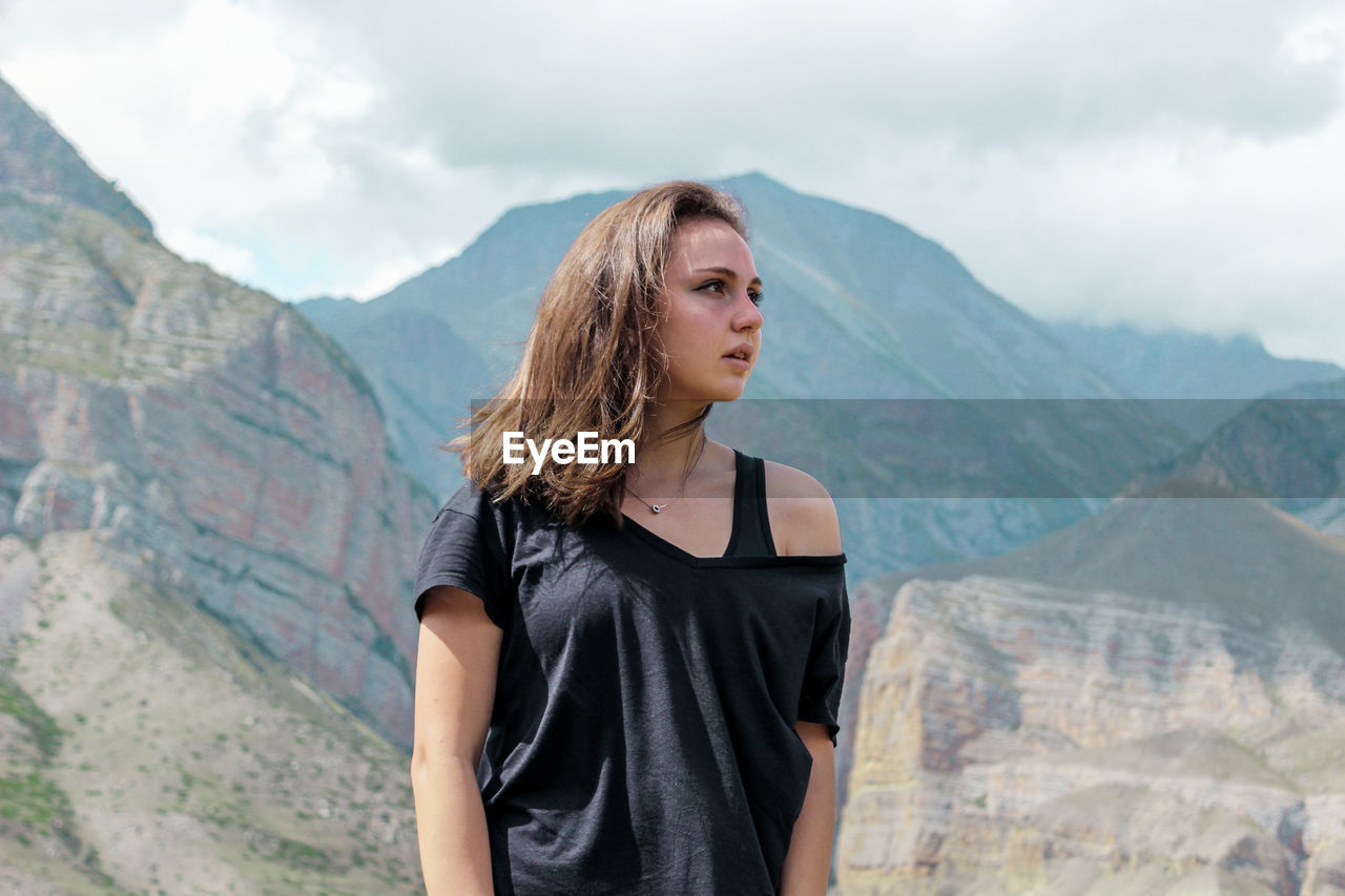 Beautiful young woman looking away while standing against mountain range