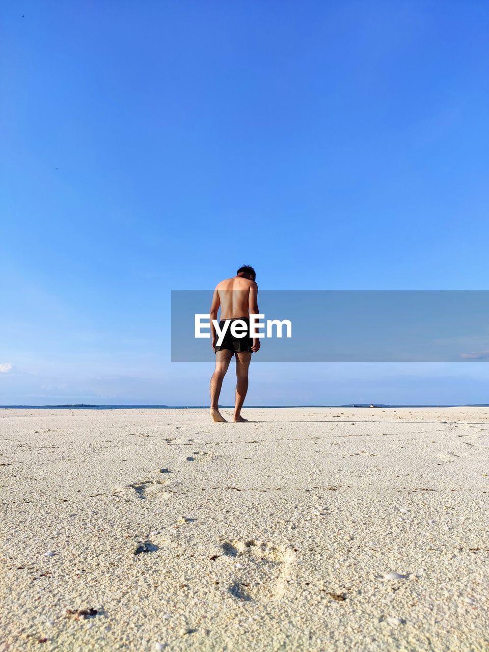 REAR VIEW OF MAN ON BEACH AGAINST SKY