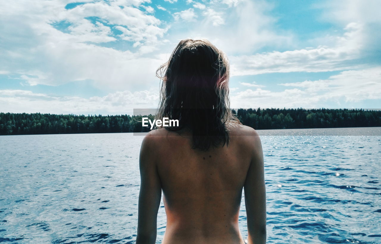 Rear view of shirtless woman by lake