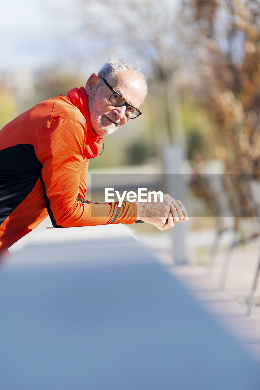 Portrait of senior man leaning on wall in park