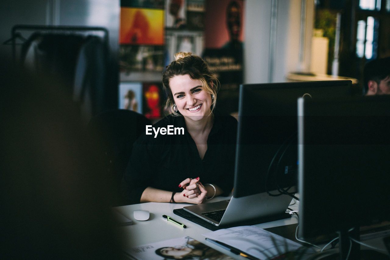 Portrait young woman smiling while sitting at desk in creative office