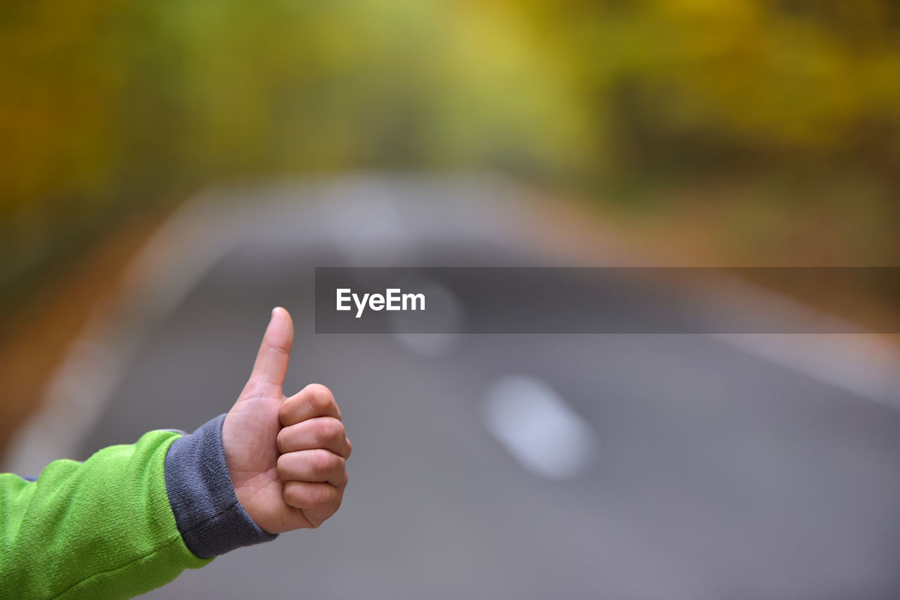 Cropped hand of child gesturing thumbs up sign over road