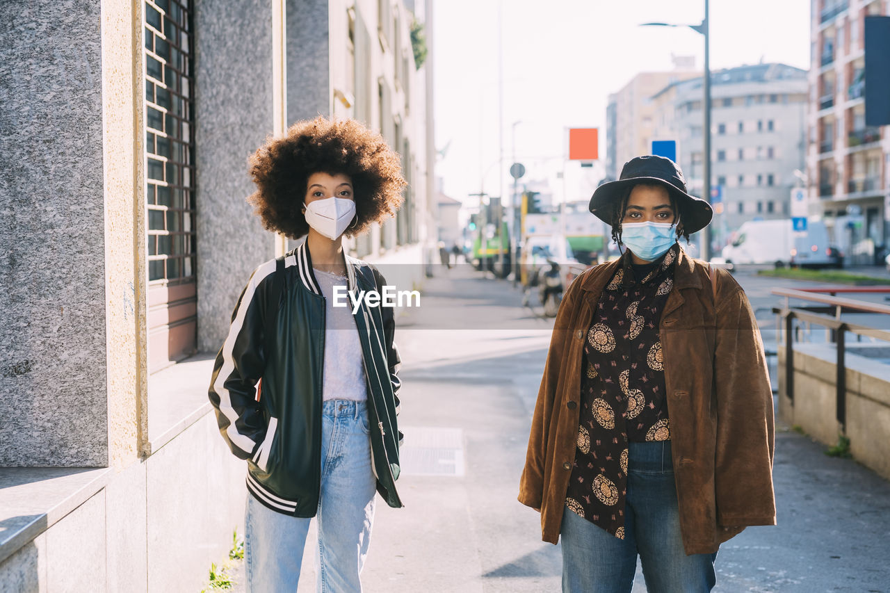 Friends wearing protective face masks standing with social distance on footpath