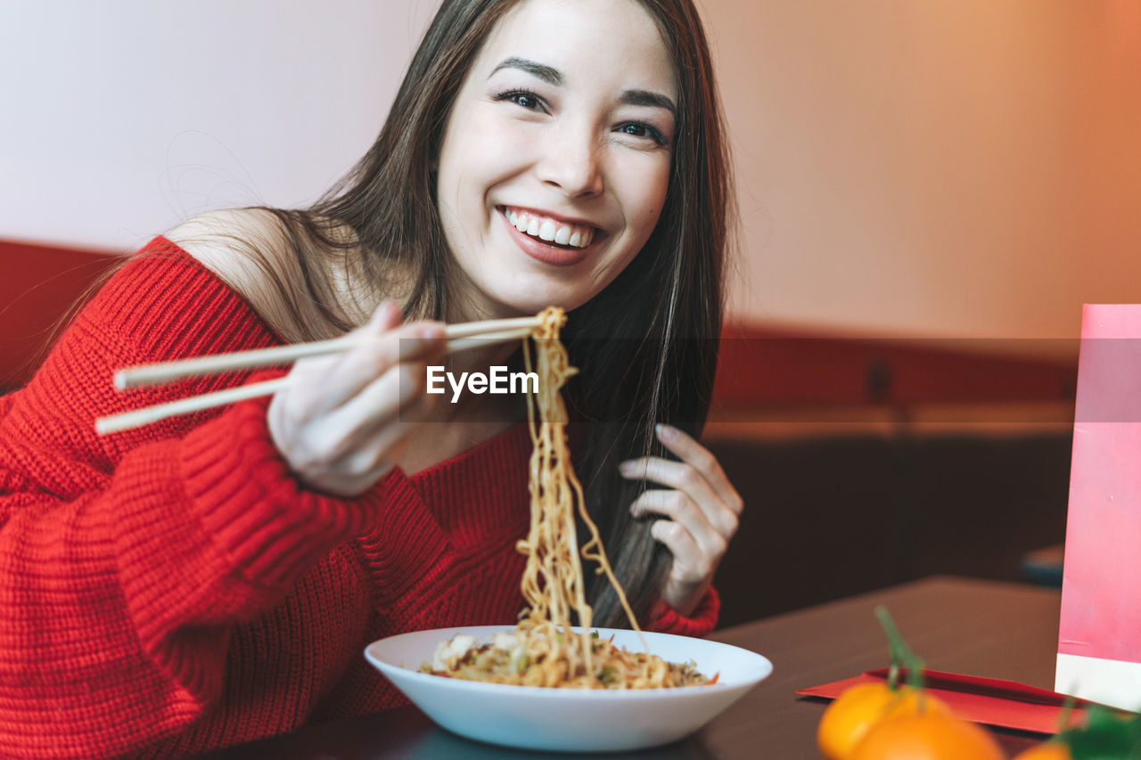 Asian woman in red clothes eating noodles with chopsticks in the chinese vietnamese restaurant