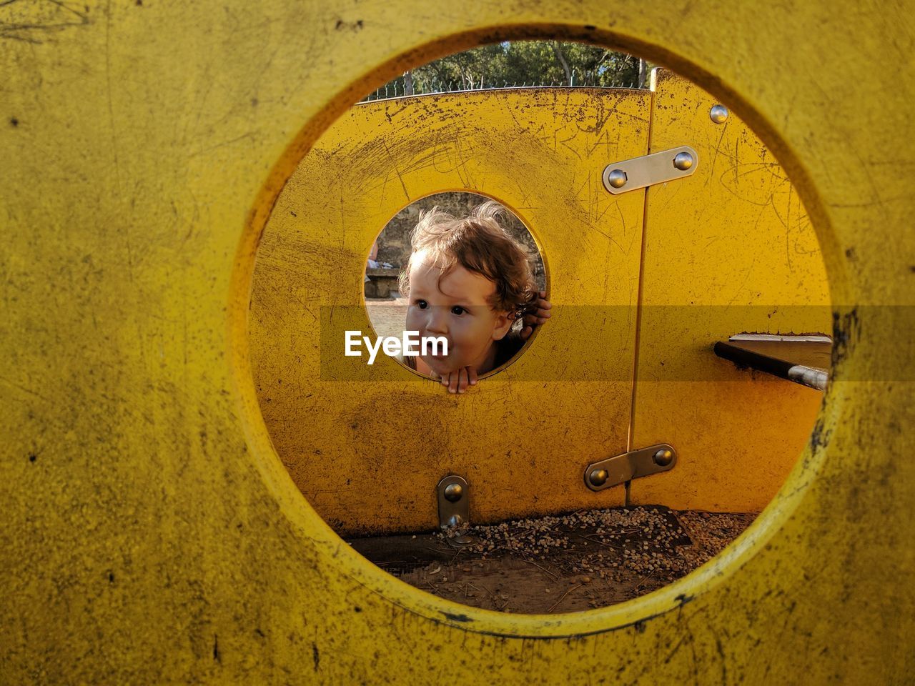Cute baby boy looking through hole of play equipment