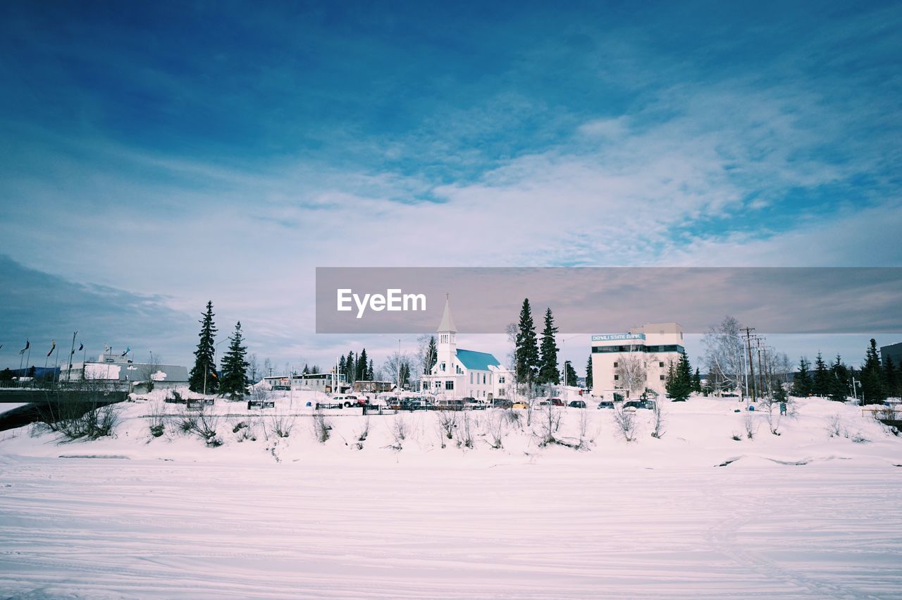 Houses on snow covered field against cloudy sky