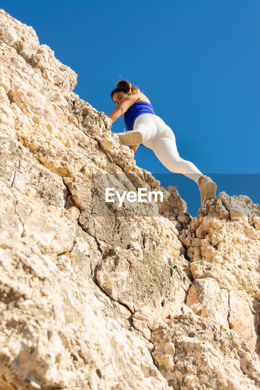Woman climbing a rocky cliff in bright sunny weather, close to the summit, latin woman, middle-aged