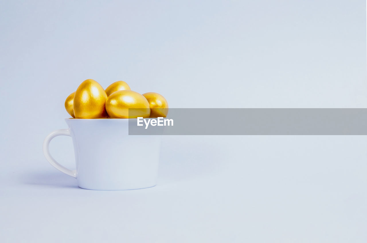 Decorative easter eggs are painted gold and stacked in a blue porcelain cup 