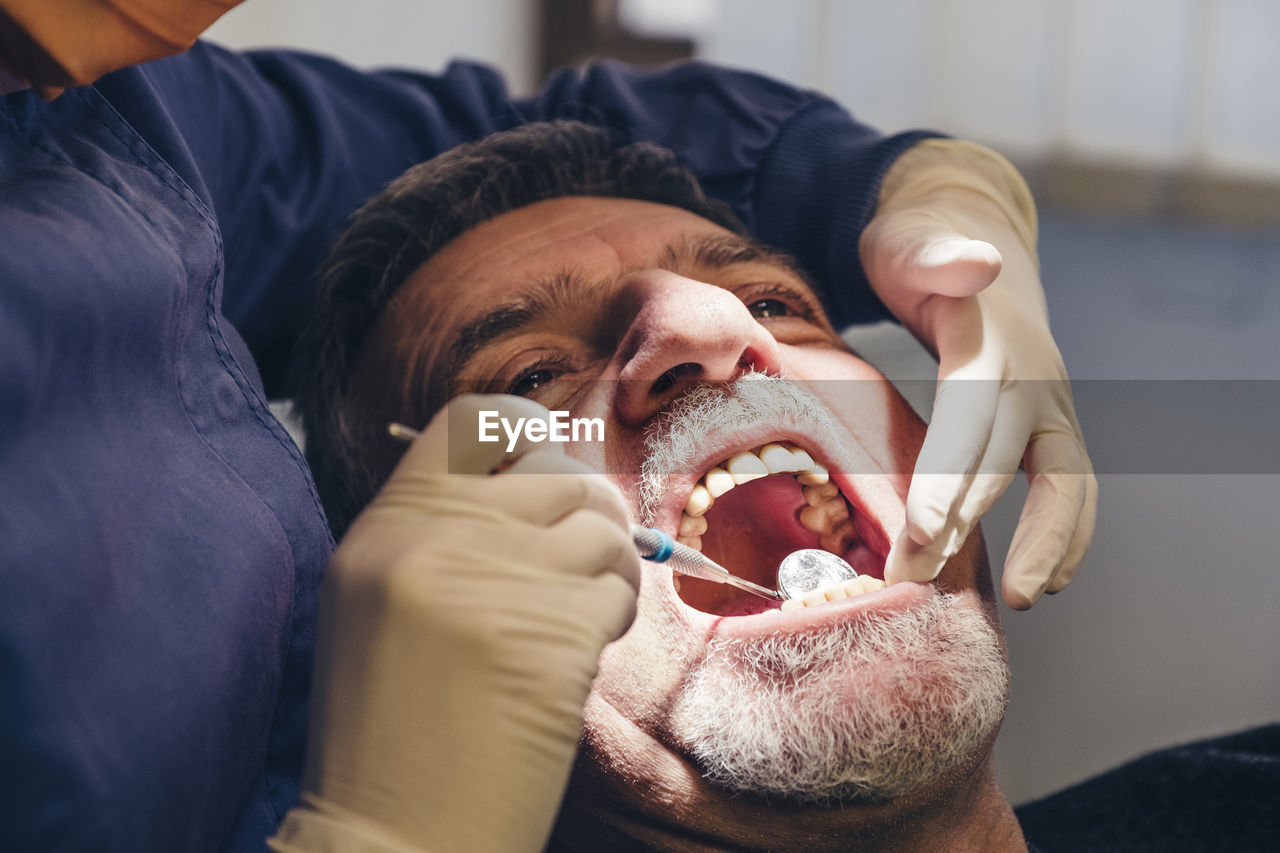 Cropped image of dentist using angled mirror while examining patient's teeth