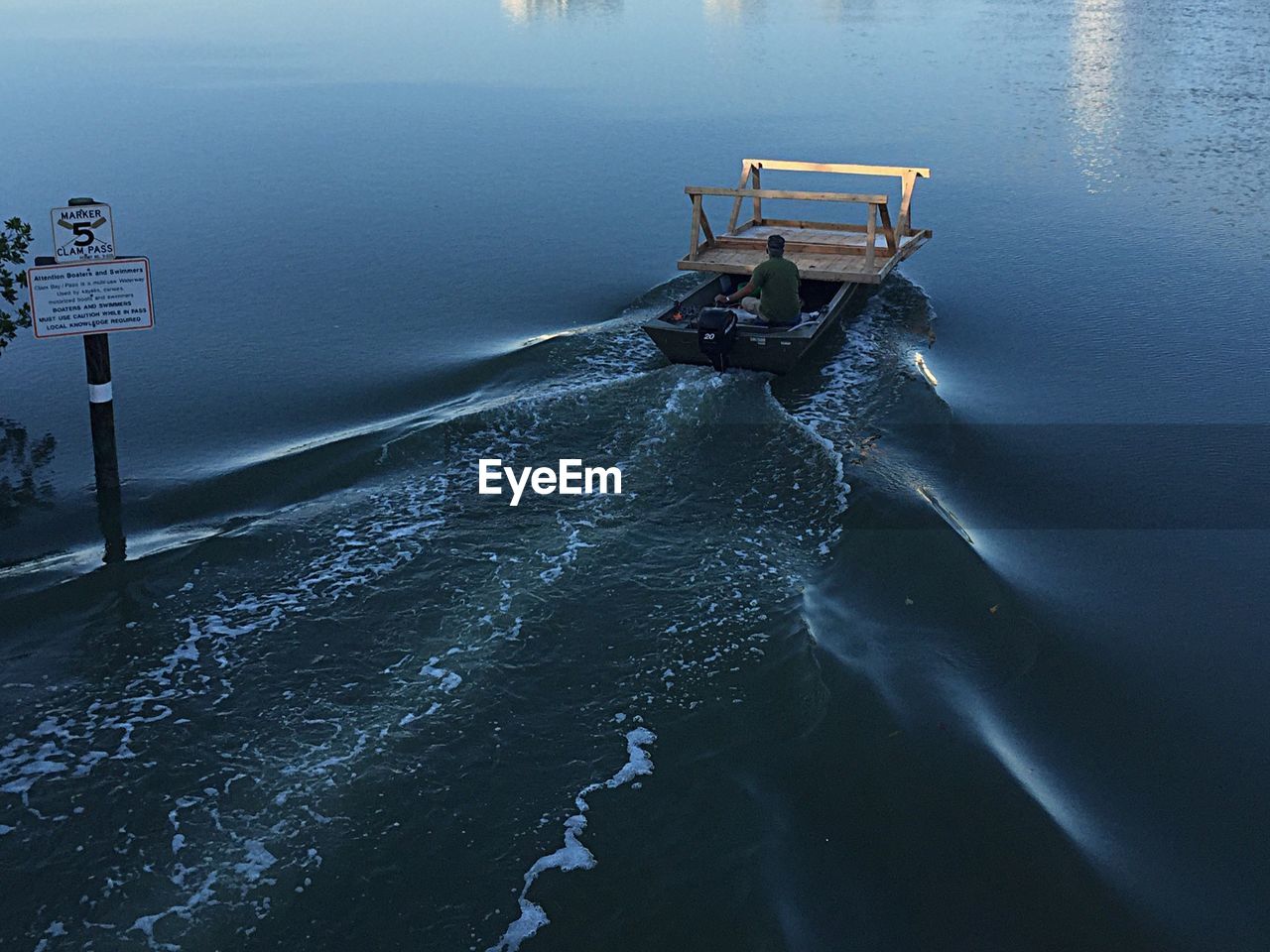 Rear view of man carrying wooden table on motorboat in water