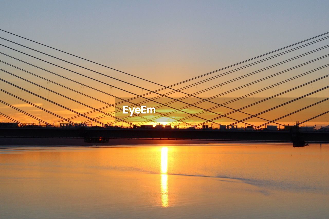 Silhouette bridge over river against sky during sunset