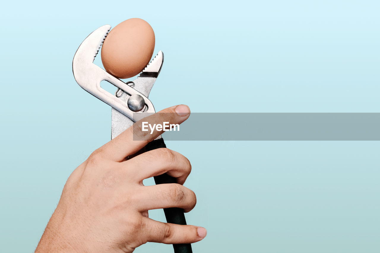 Close-up of person hand holding a spanner against white background