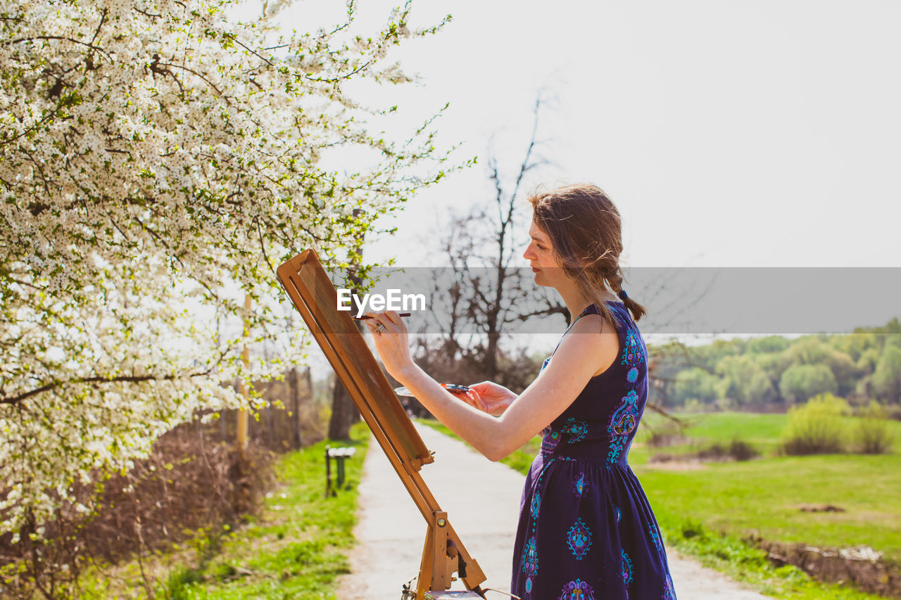 Side view of woman standing by plants against sky