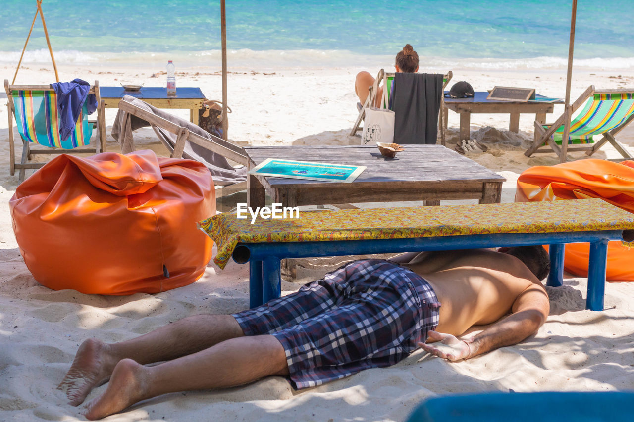 MIDSECTION OF MAN SITTING ON BEACH