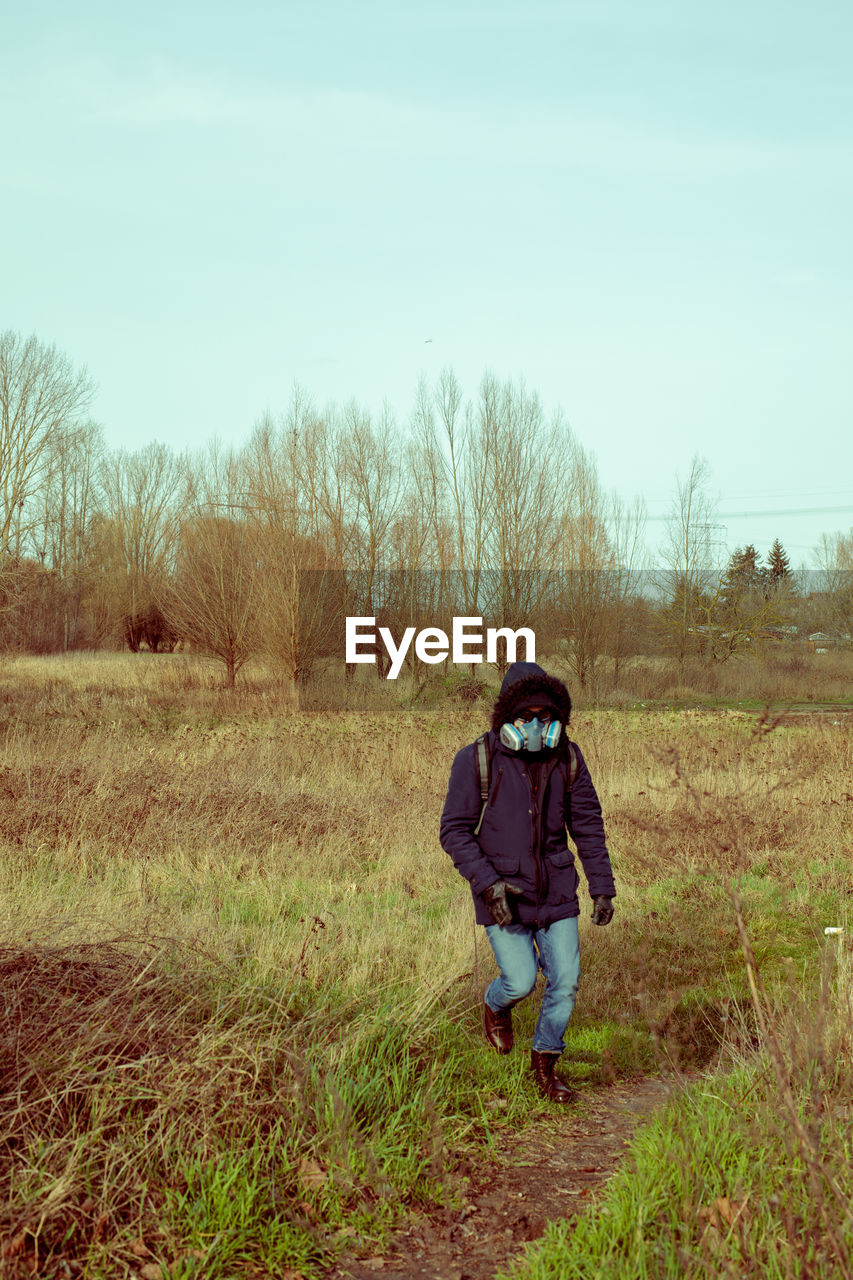 REAR VIEW OF MAN WALKING ON FIELD AGAINST SKY