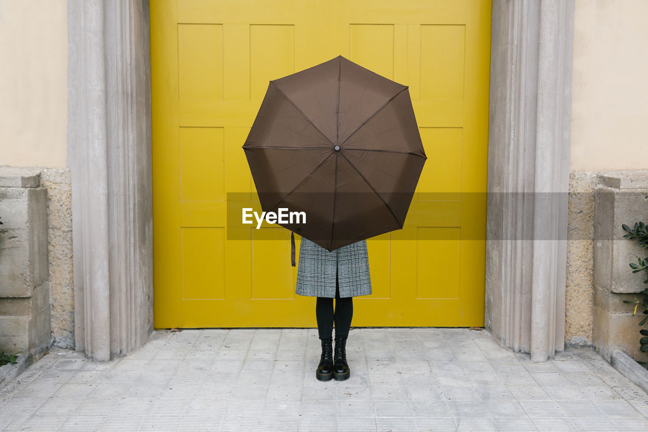 Woman holding umbrella while standing against yellow door