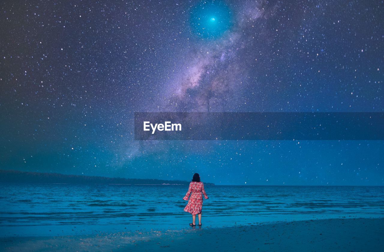 Rear view of woman standing at beach against sky at night