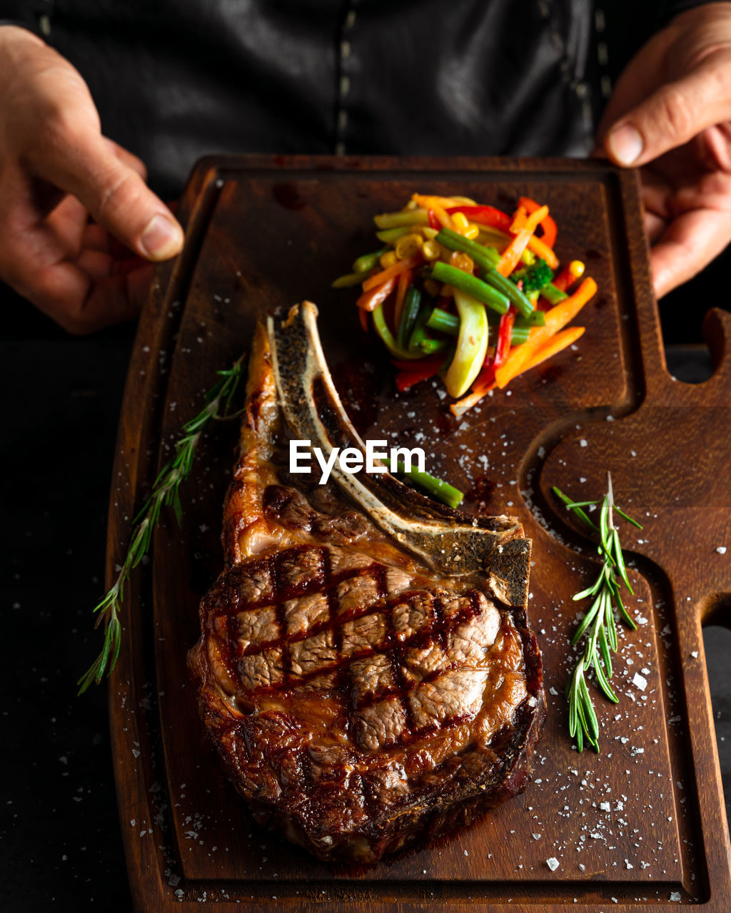Chef offering grilled steak and veggies dish served on a wooden board, low key image