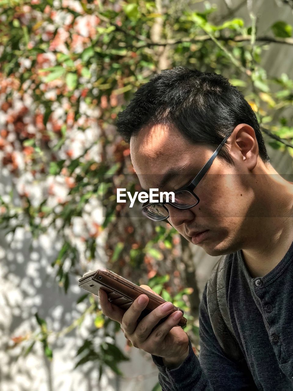 Portrait of young man with eyeglasses using mobile phone against  ivy covered wall.