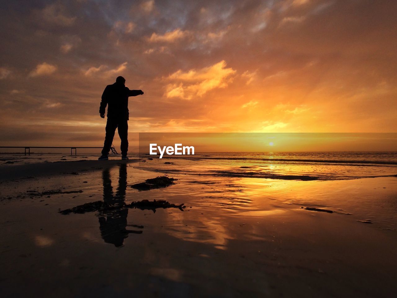 Silhouette man standing at beach against sky during sunset