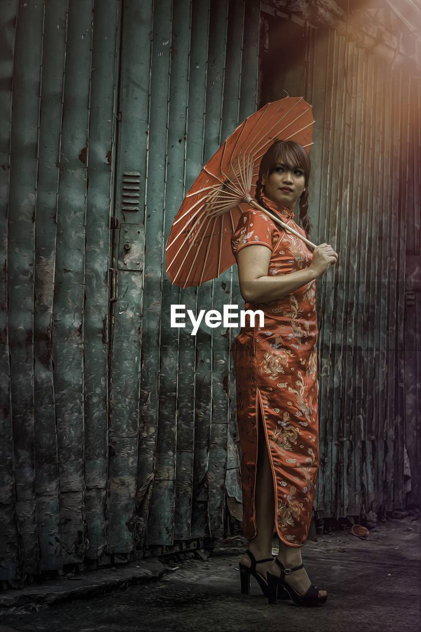 Young woman in traditional clothing holding umbrella by old shutter