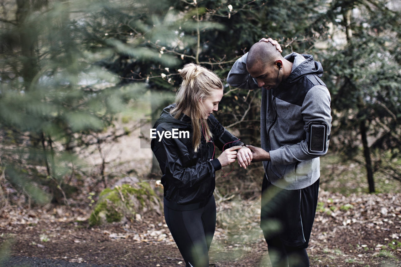 Male and female athletes checking smart watch in forest