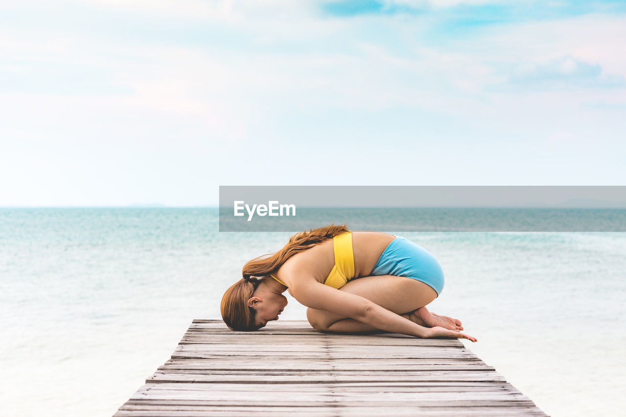 Side view of woman doing yoga on pier at beach