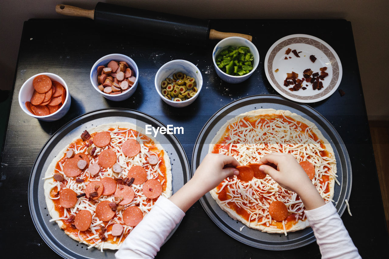 High angle view of boy's hands preparing a pizza on a table at home