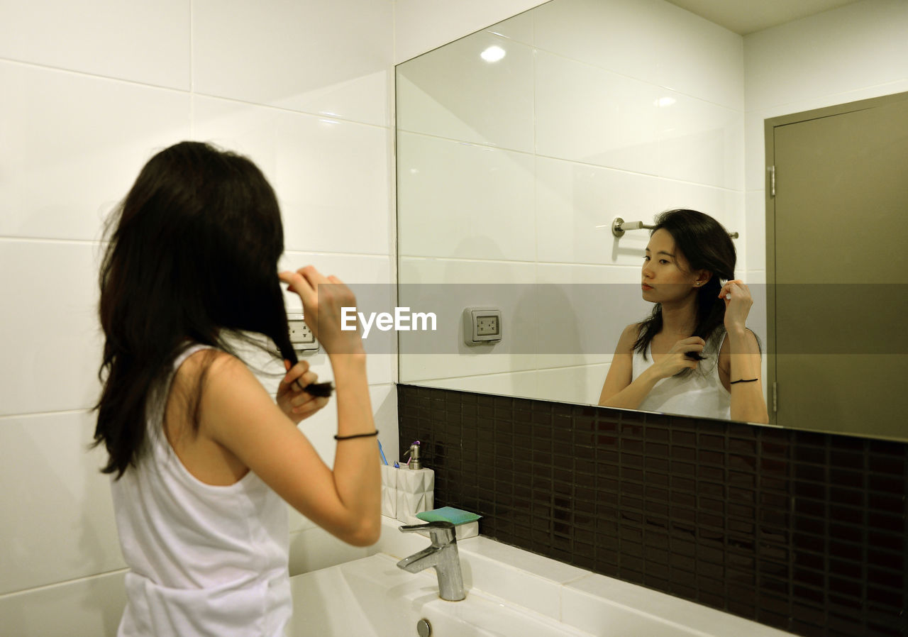 Woman making hairstyle while reflecting of mirror in bathroom