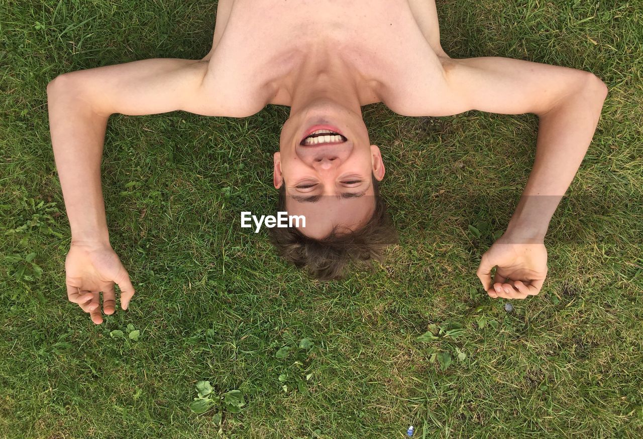 Directly above shot of happy shirtless man lying on grassy field