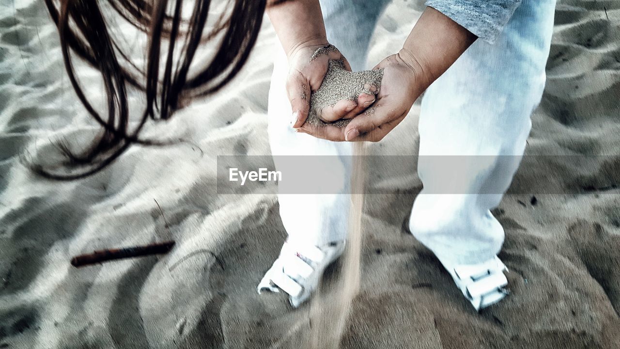 Low section of girl holding sand at beach