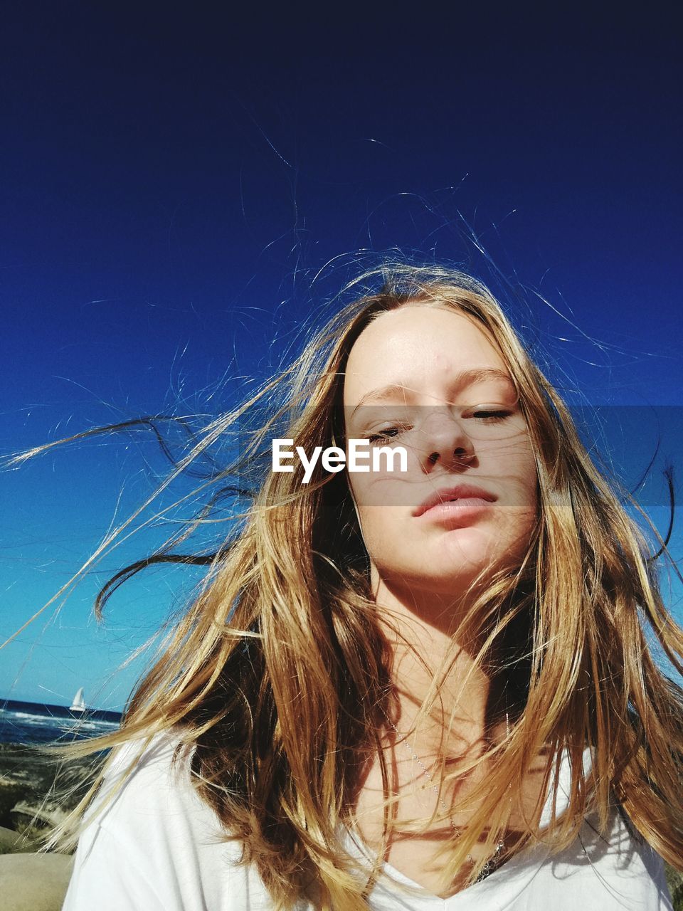 Close-up of young woman with tousled hair against clear sky