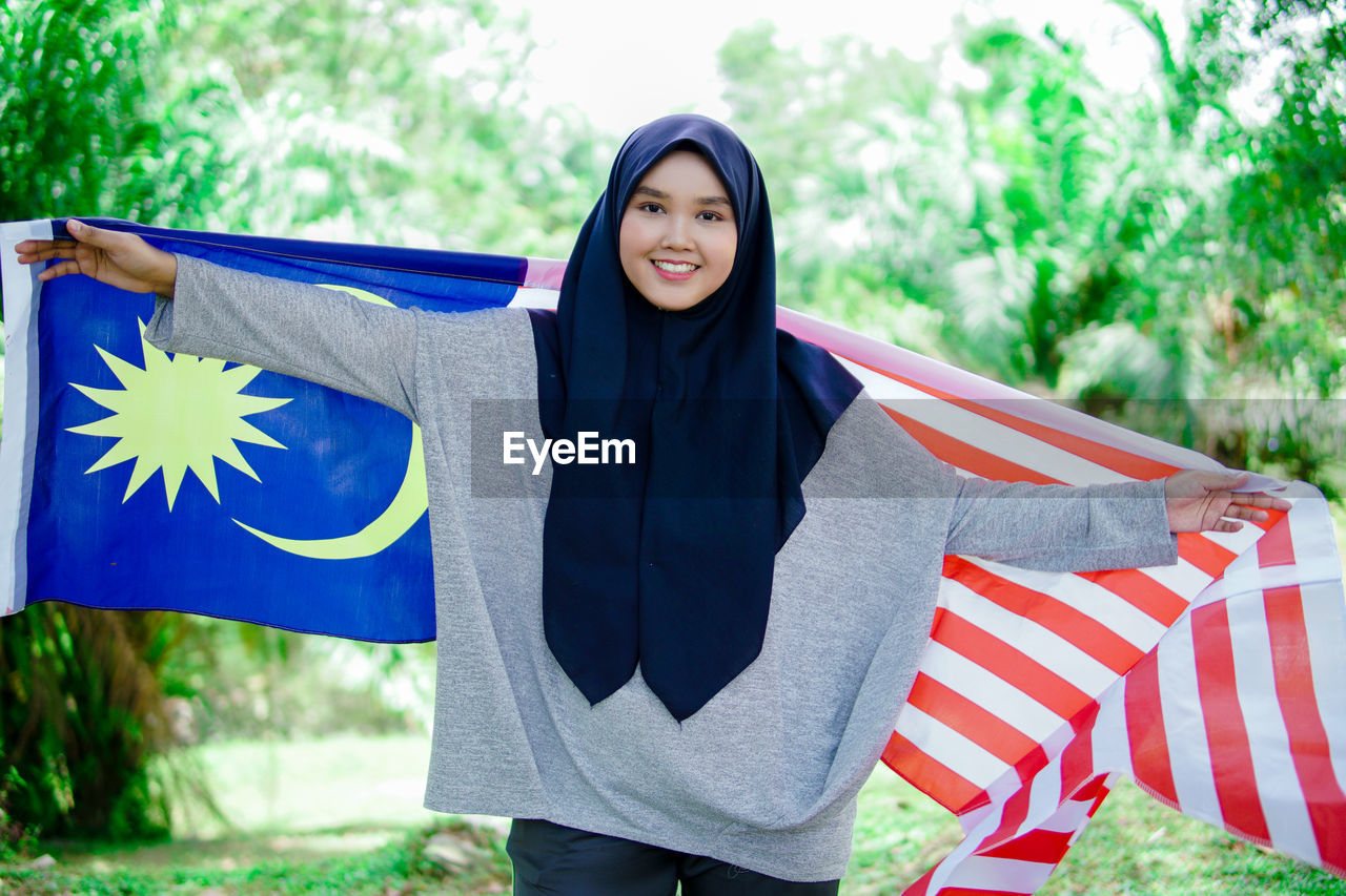 PORTRAIT OF SMILING WOMAN STANDING AGAINST BLUE SKY