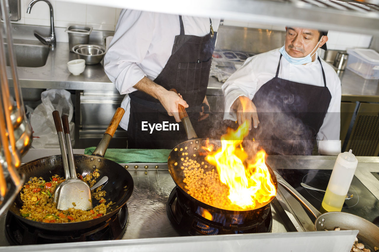 Chef teaching colleague flaming food in wok at kitchen