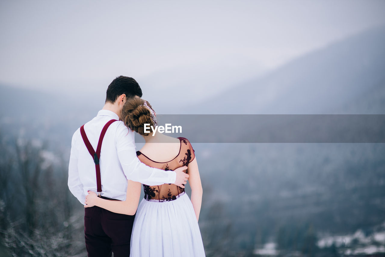 COUPLE STANDING ON MOUNTAIN AGAINST MOUNTAINS