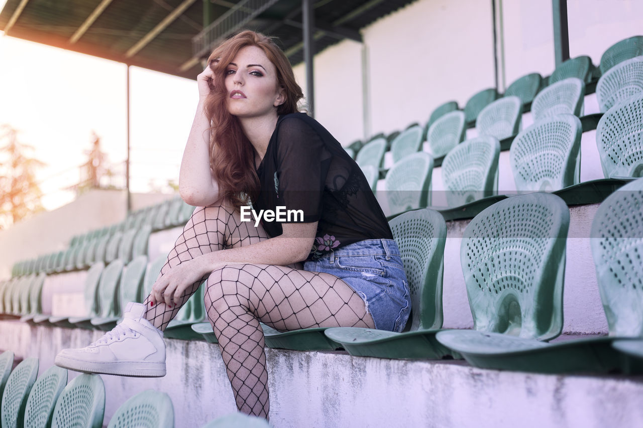 Portrait of young woman sitting on chair at stadium