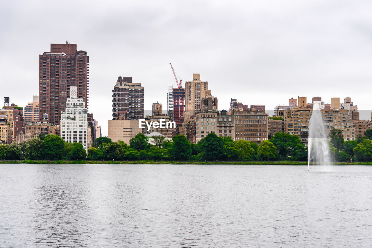 Buildings by river against sky in city