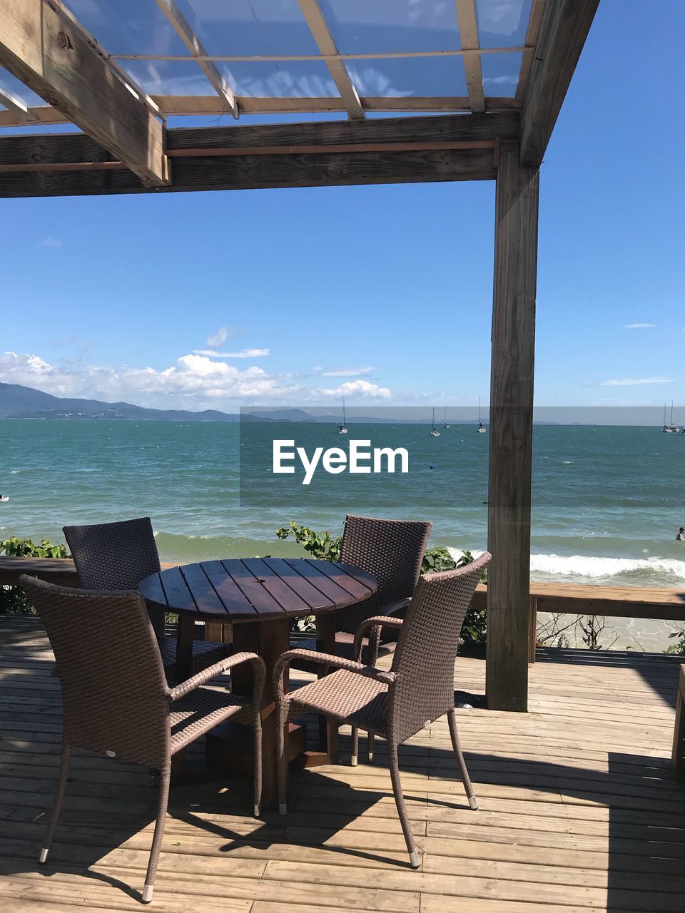 EMPTY CHAIRS AND TABLES AT BEACH AGAINST SKY